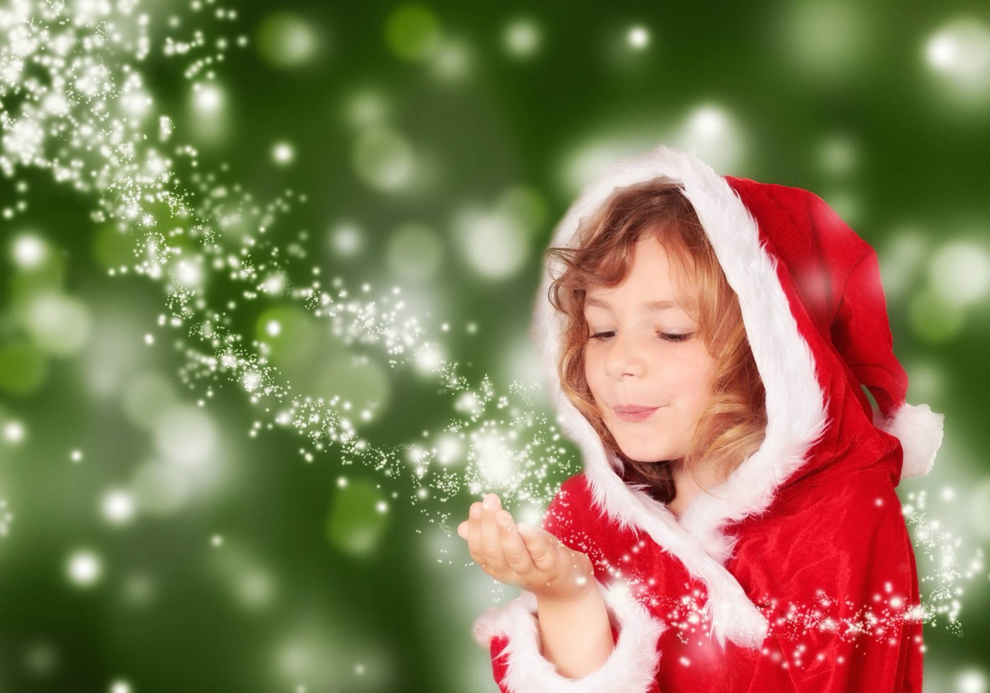 Petite fille en manteau rouge de Noël soufflant une poussière d'étoiles au creux de sa main